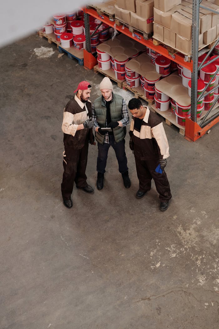 Three workers discussing logistics in a warehouse with shelves stocked with products.