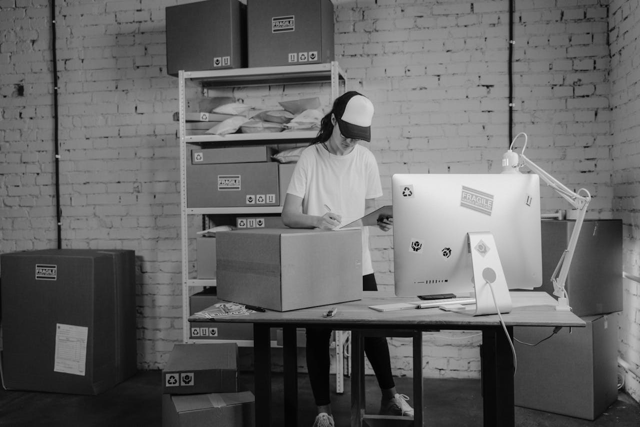 A woman handling packages in a monochrome office setting, focused on organizing shipments and logistics.