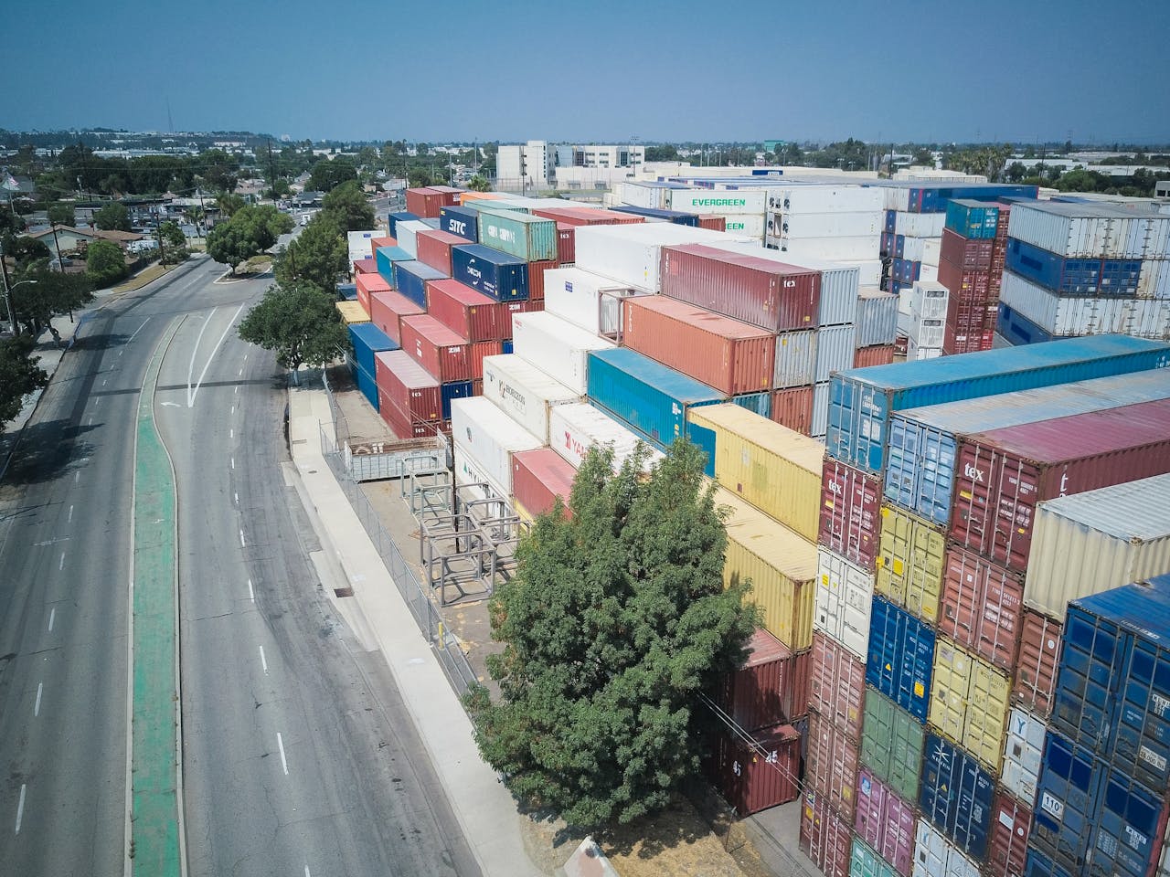 Drone shot showcasing an organized stack of colorful shipping containers by an empty road.